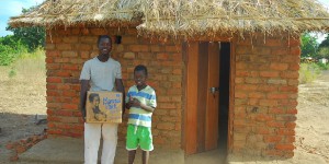 two Malawai boys standing in front of a hut holding a Manna Pack