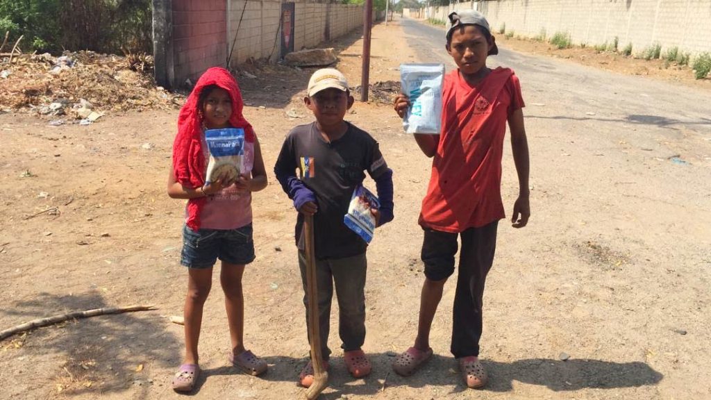 Three Venezuelan children carry manna packs home to provide much-needed meals.